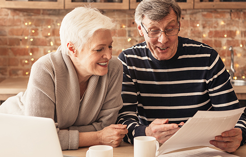 Smiling Senior Couple Reading Health Insurance Policy Contract In Kitchen Together