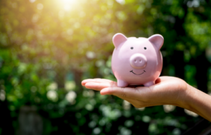 Pink piggy bank resting on a lady's hand with blurry green leafy background
